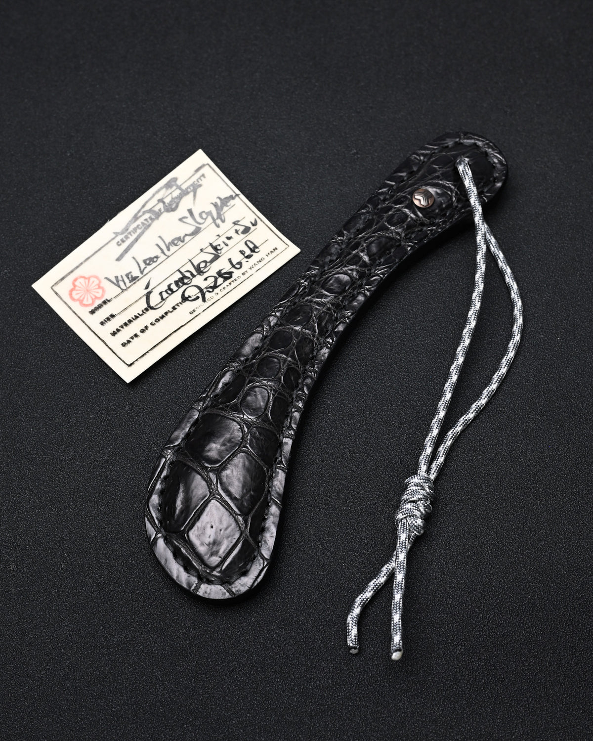 Sunizumi Shoten × Wtopia black crocodile leather EDC paddle featuring genuine crocodile leather, internal steel plate, bronze emblem with silver inlay, and 550 paracord lanyard, made in Japan